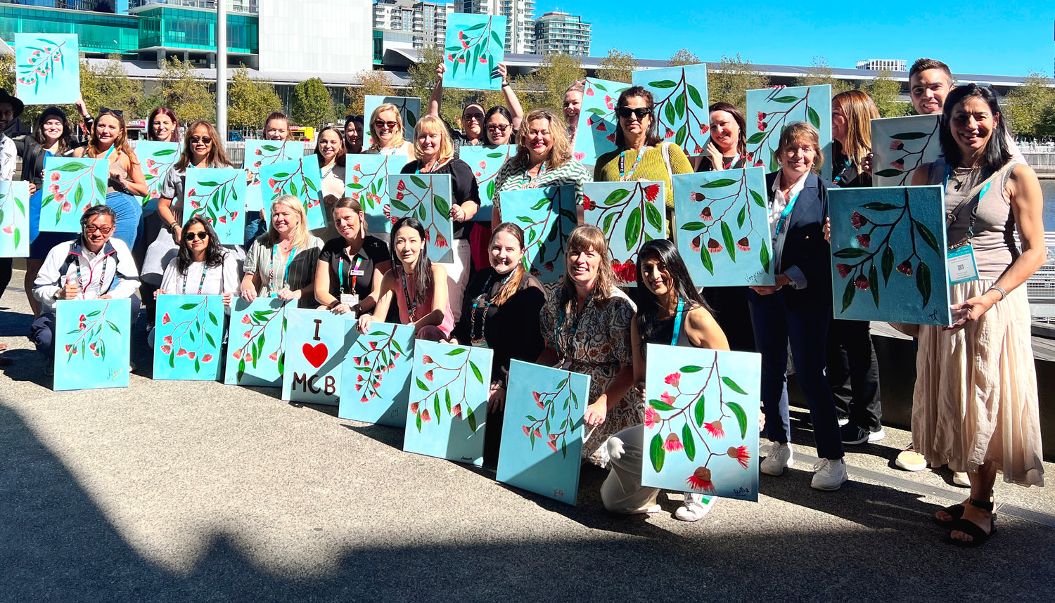 Group of people holding painted canvases with various designs outdoors.