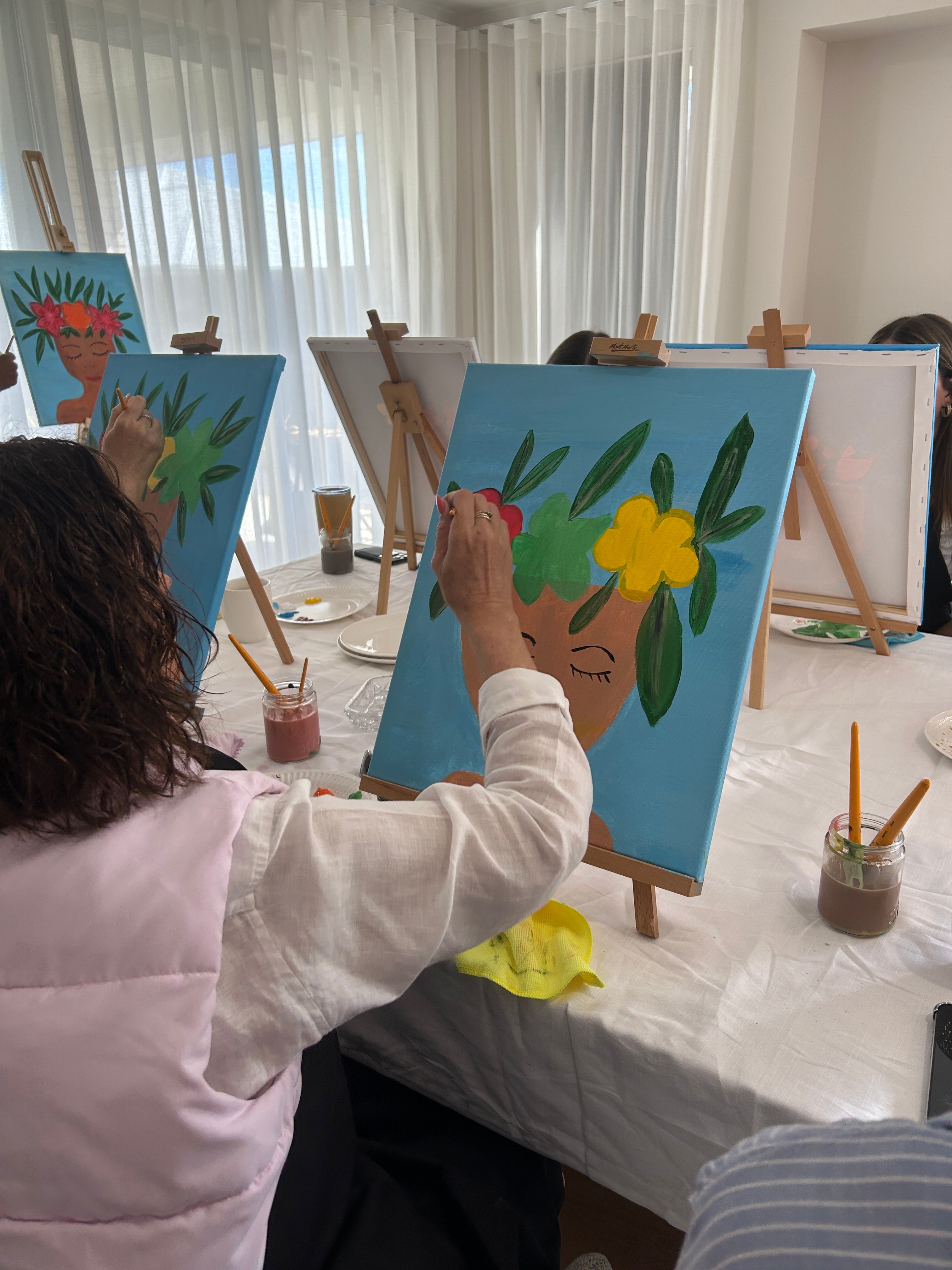 Group of people painting on canvases with a focus on a person in a white jacket.