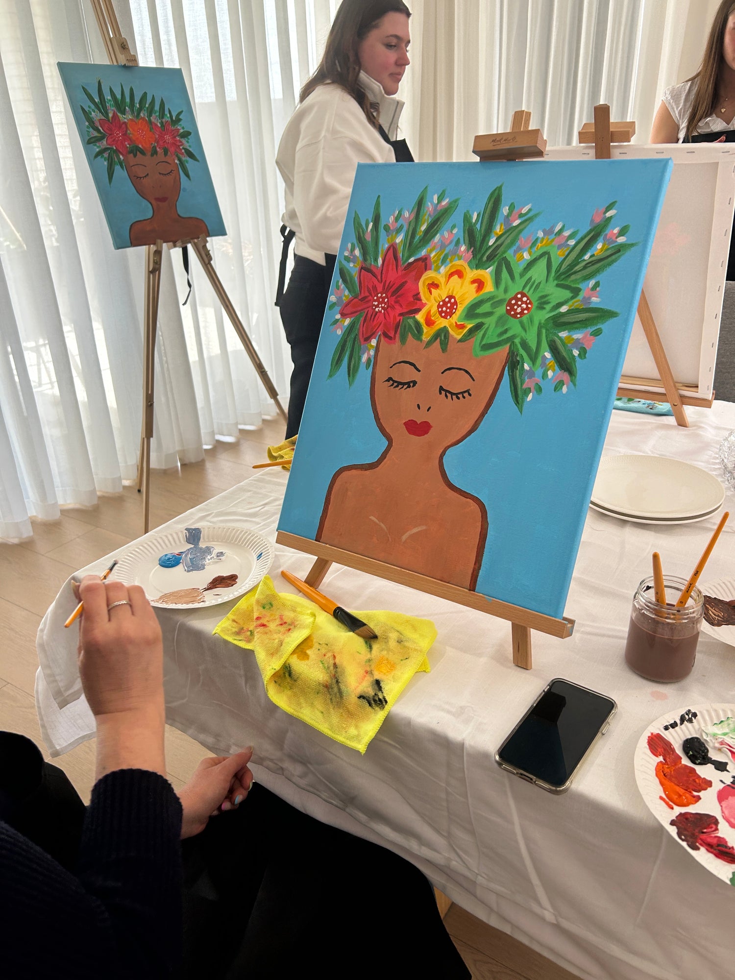 Artistic painting session with a completed artwork of a woman's face with flowers on a table.