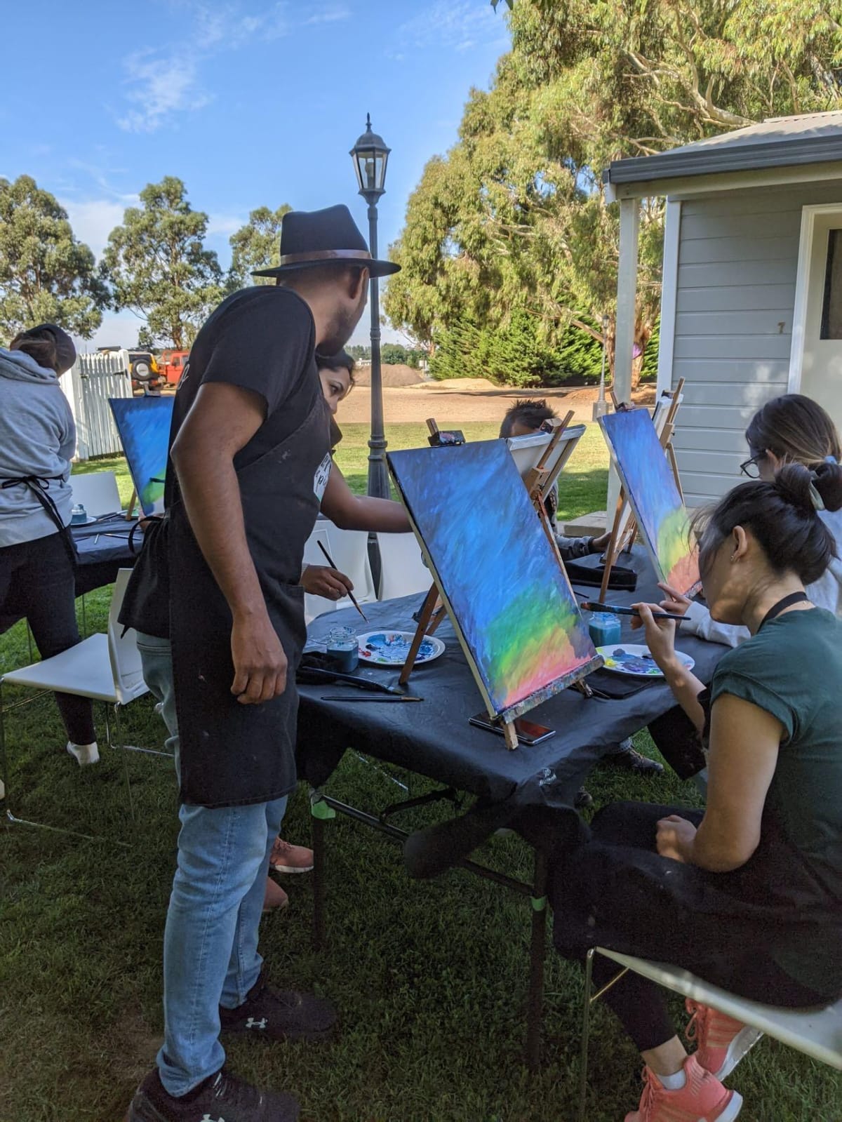 Group of people painting outdoors with colorful canvases.