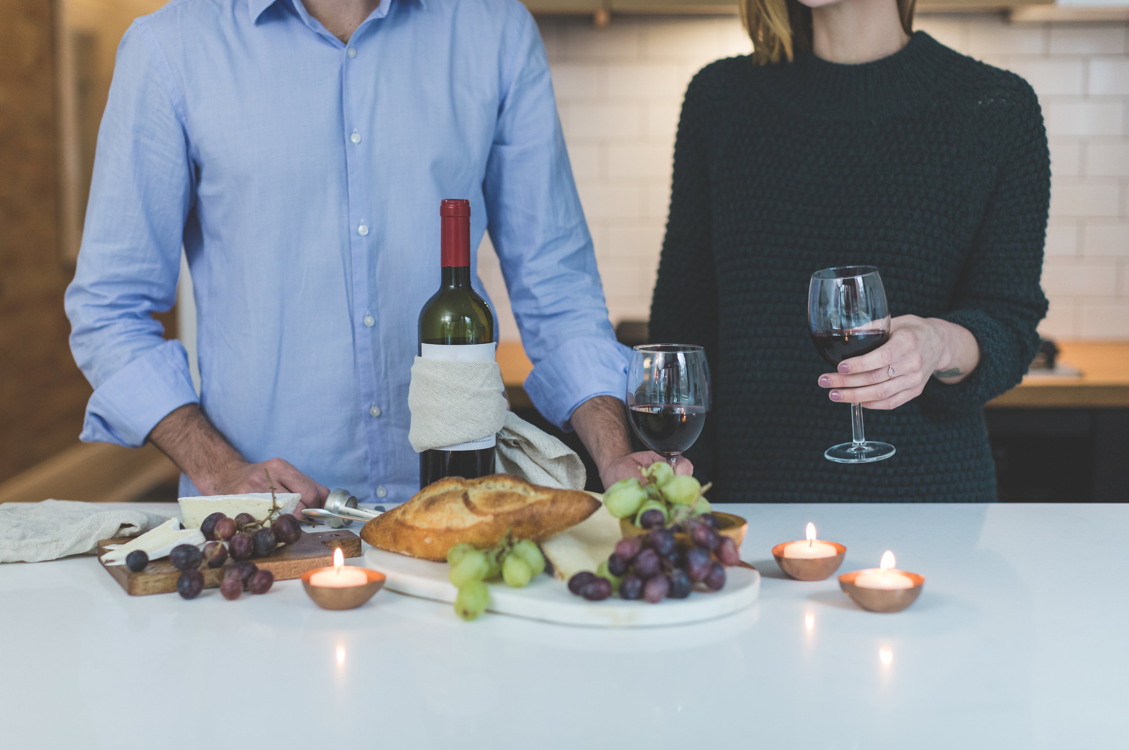 man in pale blue shirt and woman in black jumper sharing a glass of red wine and a grazing platter
